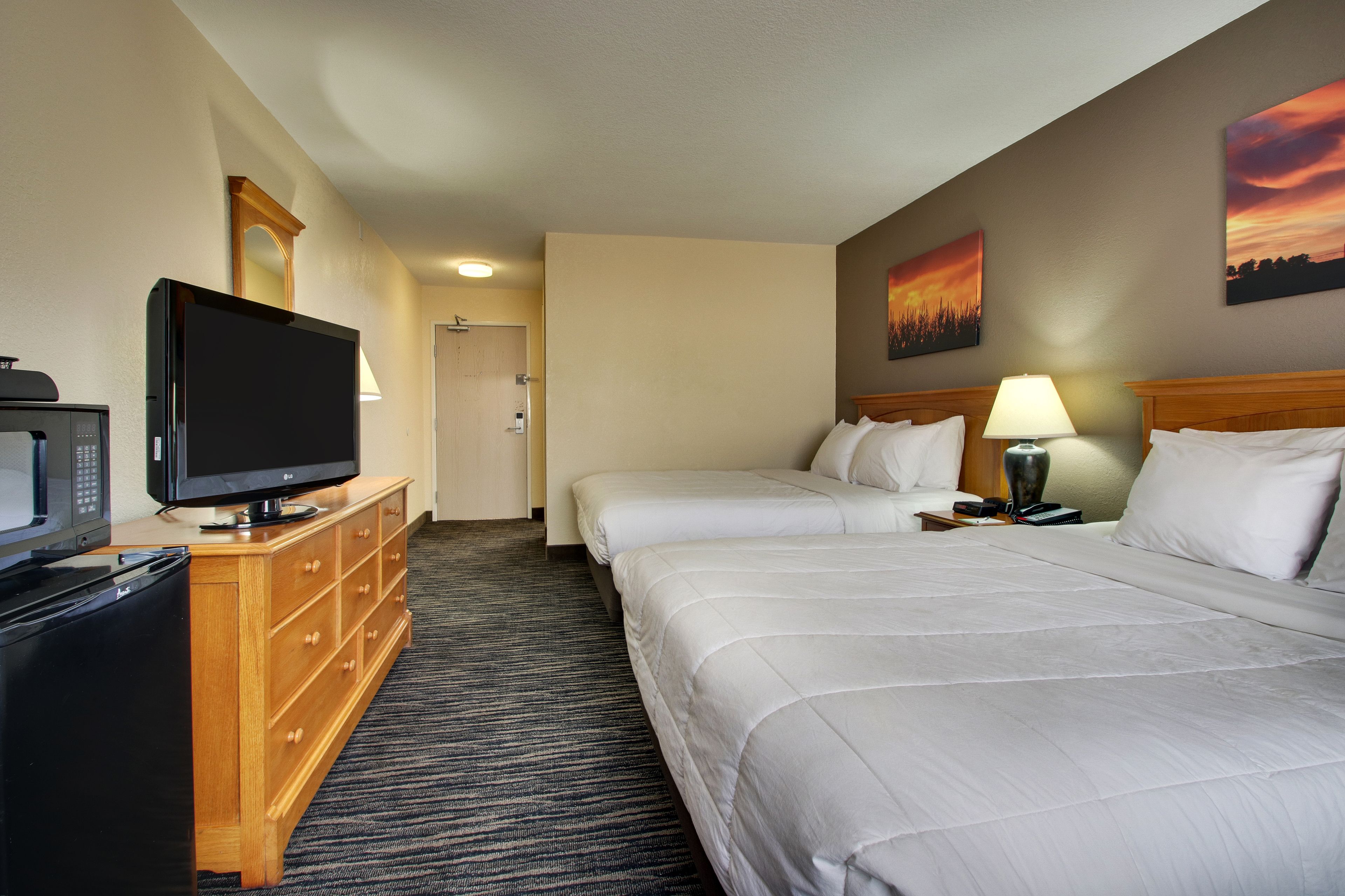 A hotel room with two beds, a TV, a wooden dresser, and a painting of a sunset.