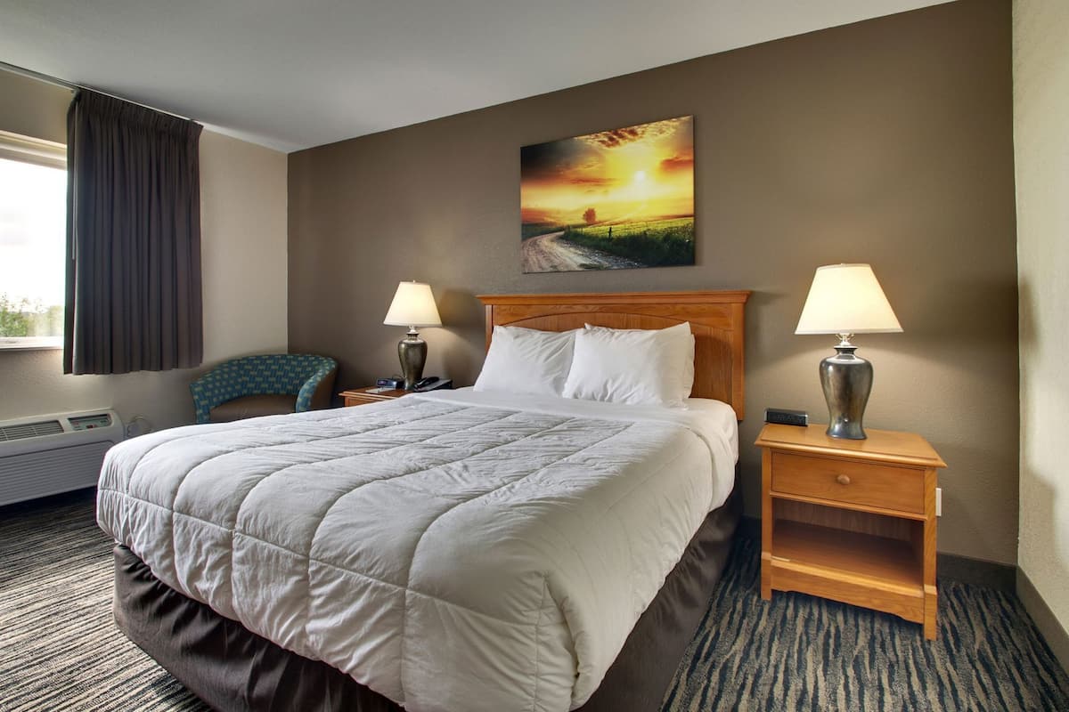 Un cuarto de hotel con una cama grande, dos lámparas de noche, una mesita de noche, una silla y un cuadro en la pared.