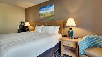 A hotel room with a large bed, two bedside tables with lamps, a small desk, and a chair with a patterned cover.