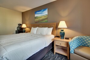 A hotel room with a large bed, two bedside tables with lamps, a small desk, and a chair with a patterned cover.