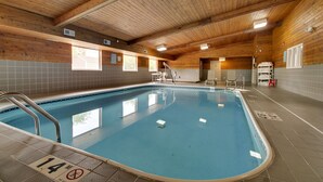 Una piscina interior con vigas de madera en el techo, paredes enlosadas y un área de piscina transparente.