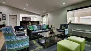 Un área de estar moderna con un sofá, dos sillones estampados, una mesita de centro y un otoman verde brillante.