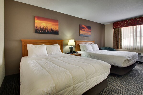 A hotel room with two beds, a nightstand with a lamp, and two paintings on the wall.