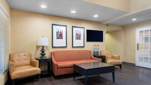 A hotel lobby with a sofa, two armchairs, a coffee table, a lamp, framed pictures on the wall, and a flat-screen TV. - Southpoint Suites Jacksonville (Jacksonville)