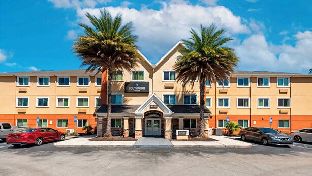 A hotel with a central entrance, palm trees, and multiple windows. - Southpoint Suites Jacksonville (Jacksonville)