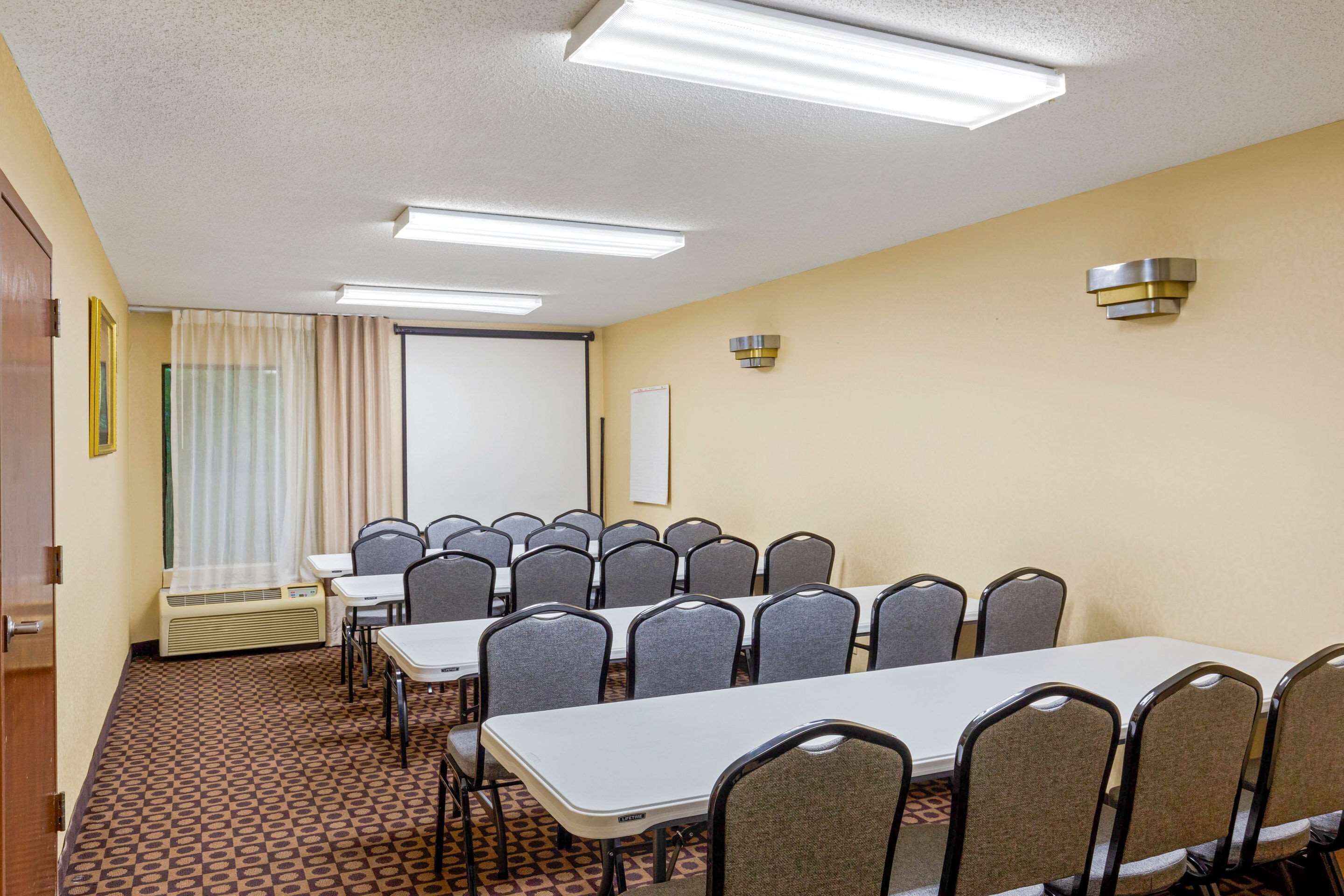 Une salle de conférence équipée d’une longue table et de nombreuses chaises, d’un écran de projection et d’un tableau blanc.