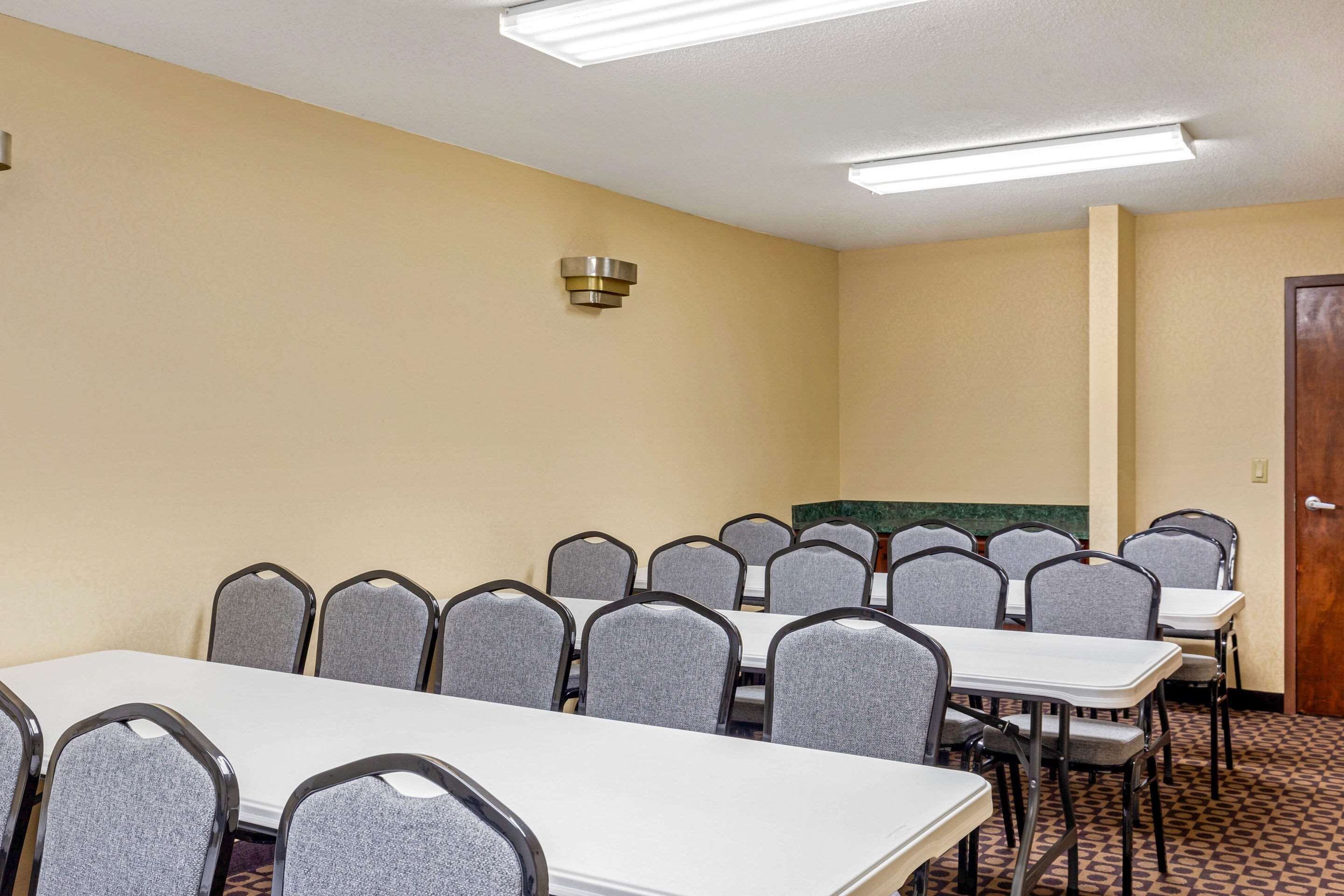 A conference room with multiple tables and chairs, a ceiling light, and a door.