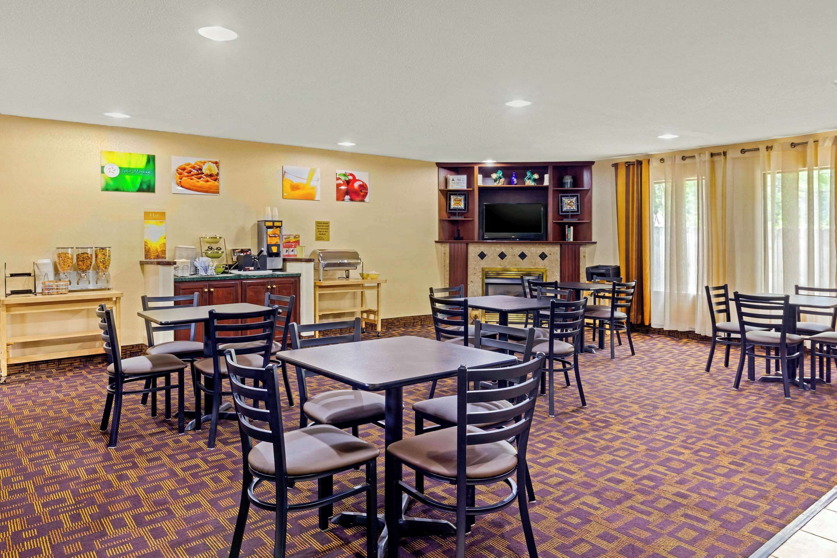 A hotel dining area with multiple tables and chairs, a coffee station, and a television on the wall.