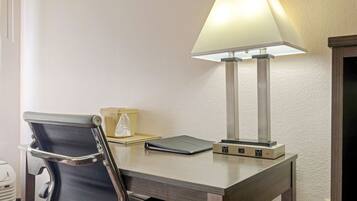 A hotel room desk with a chair, a lamp, a power strip, and a small box.