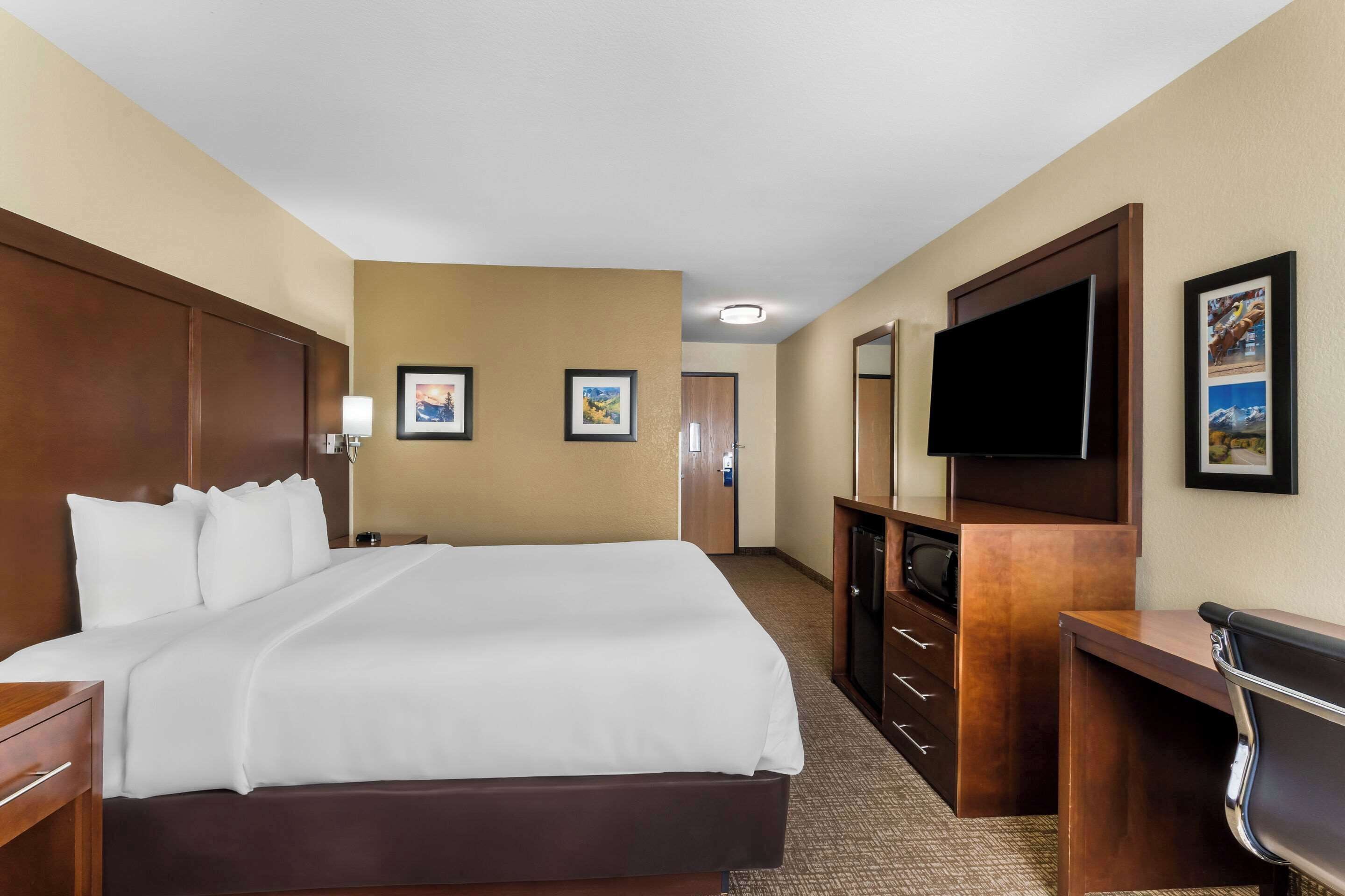 A hotel room with a large bed, a desk with a chair, a flat-screen TV, and a door leading to a bathroom.