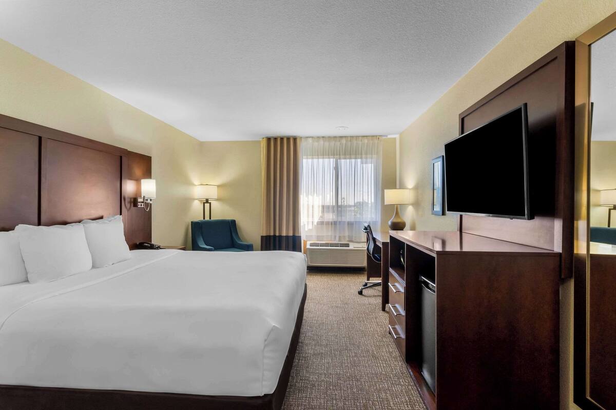 A hotel room with a large bed, a desk with a chair, a television, and a window with curtains.