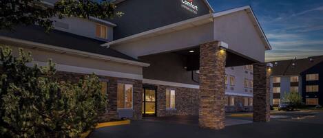 A hotel exterior with a prominent 'Comfort Inns & Suites' sign, a covered entrance, and a brick facade.