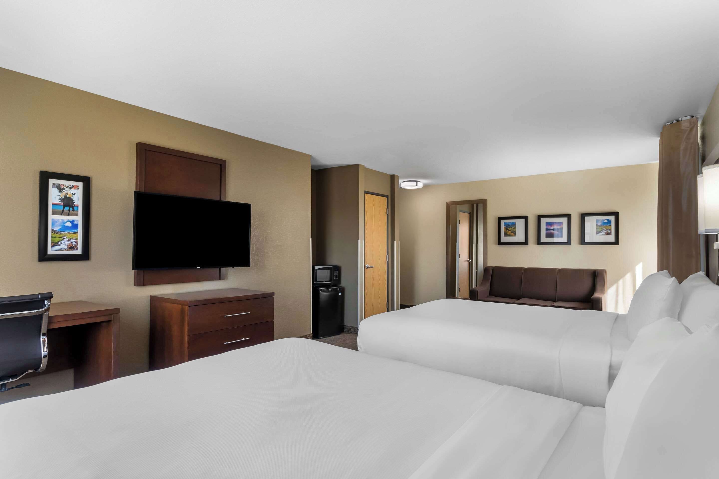 A hotel room with two beds, a TV, a desk, and a minibar.