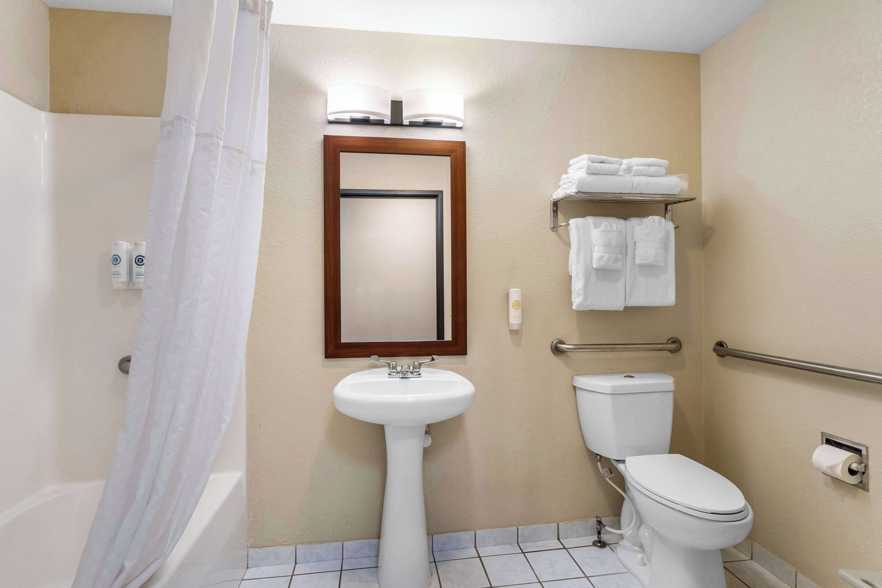 A bathroom with a pedestal sink, a toilet, a shower with a curtain, and a towel rack with folded towels.