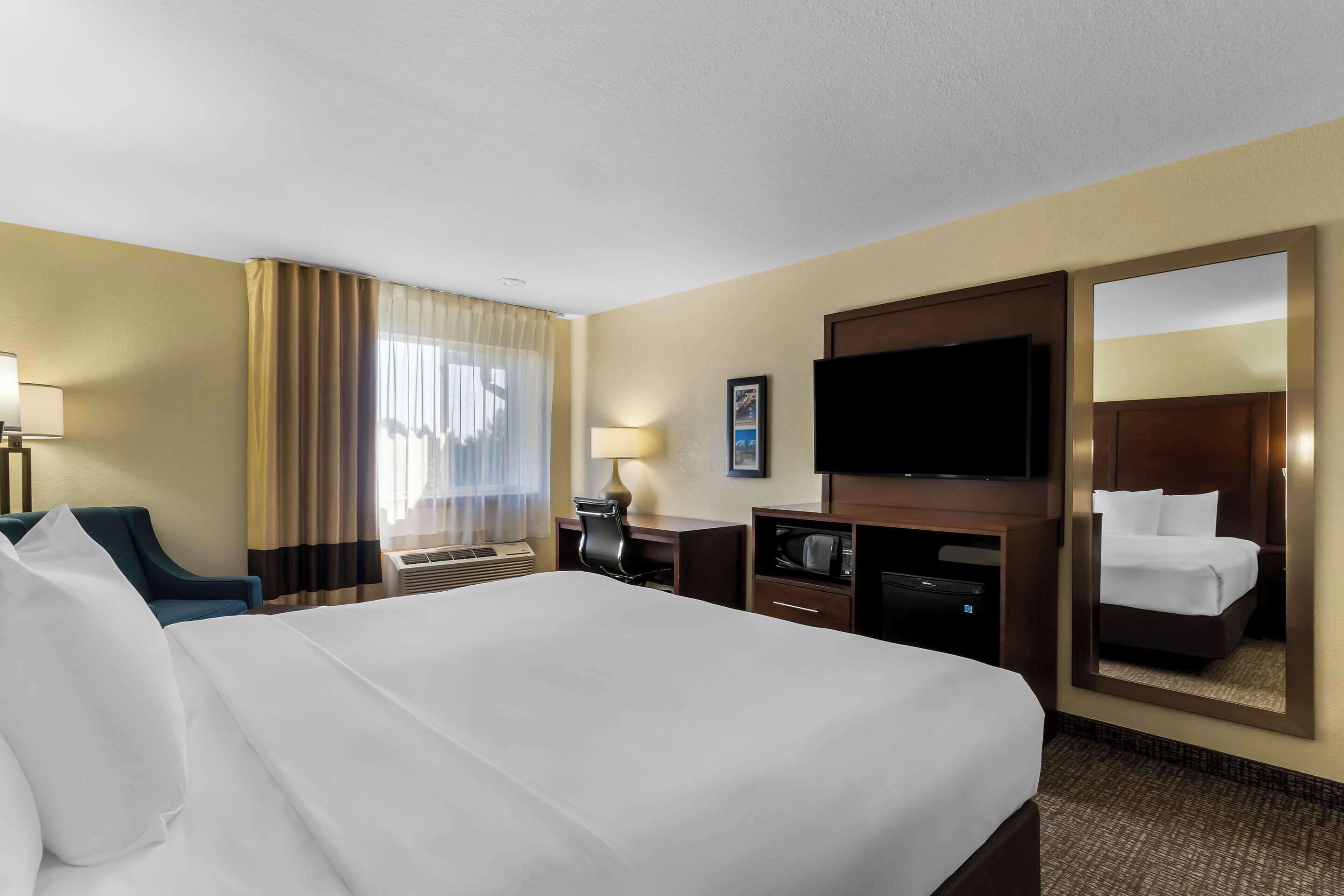 A hotel room with a large bed, a desk with a chair, a television, and a mirror.