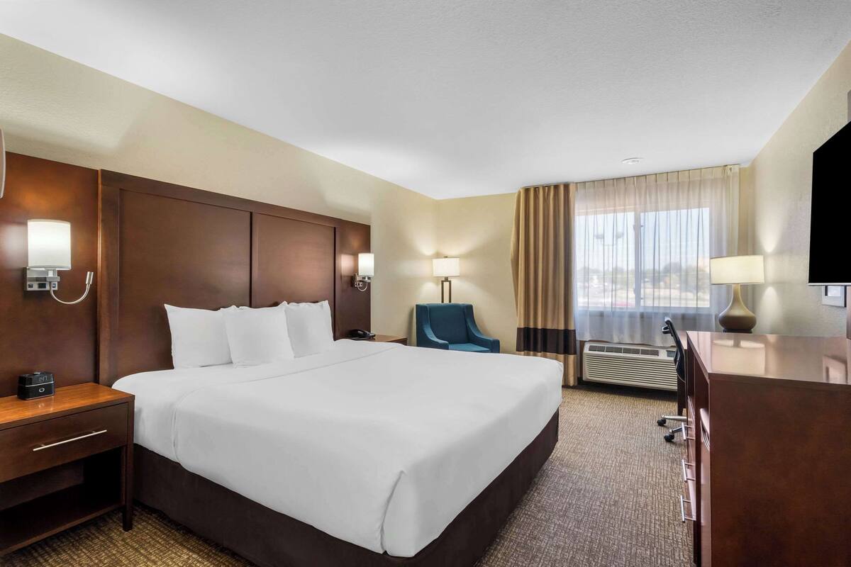 A hotel room with a large bed, a desk, a chair, a TV, and a window with curtains.