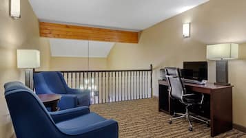 A hotel room with a balcony, a desk with a computer, two blue armchairs, and a patterned carpet.