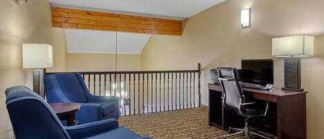 Une chambre d’hôtel avec un balcon, un bureau avec un ordinateur, deux fauteuils bleus et une moquette à motifs.