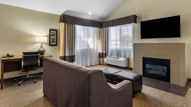 Ein Hotelzimmer mit einer Couch, einem Schreibtisch mit Lampe, einem Flachbildfernseher, einem Kamin und großen Fenstern mit Vorhängen.