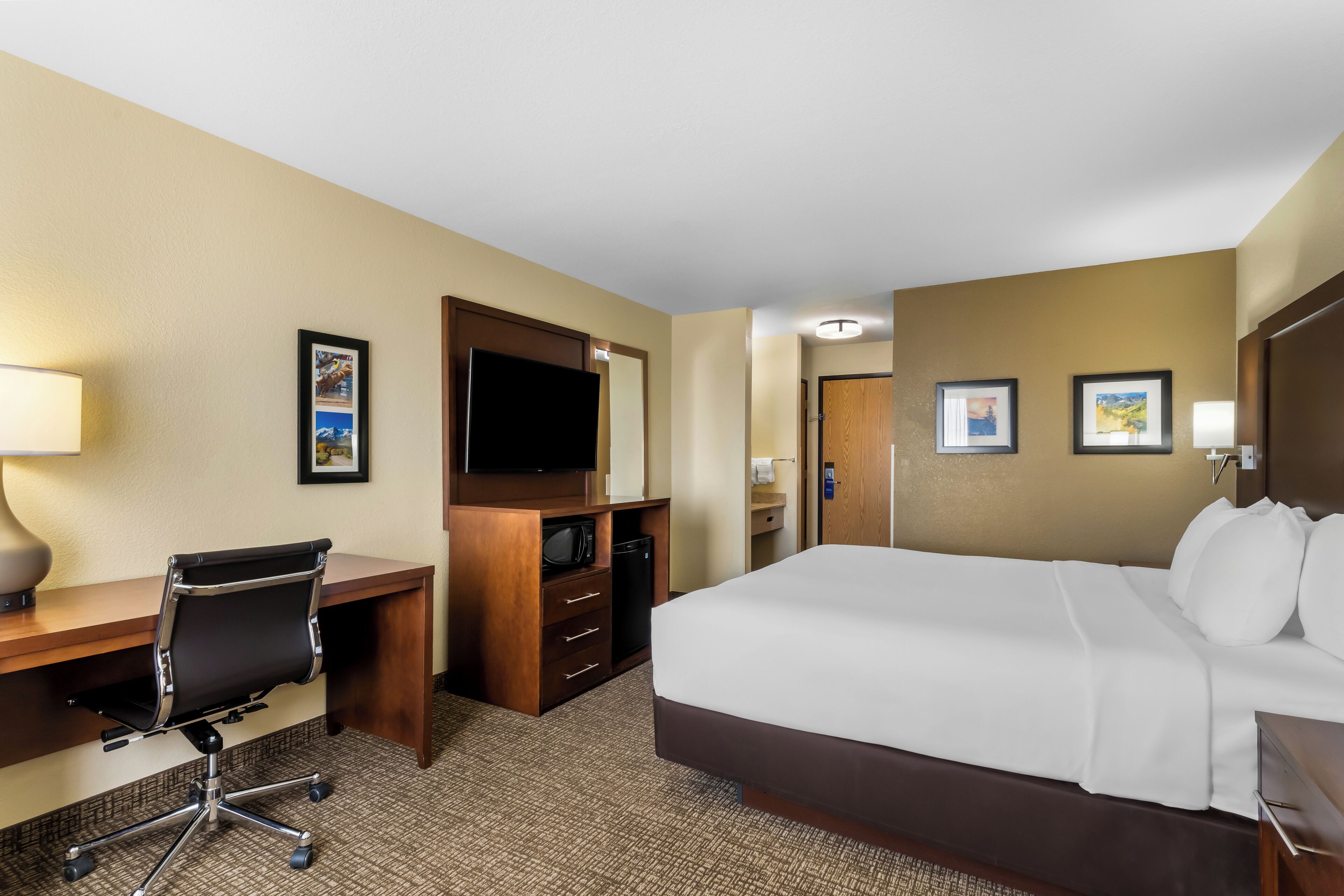 Ein Hotelzimmer mit Bett, Schreibtisch, Stuhl, Fernseher und Bildern an den Wänden.