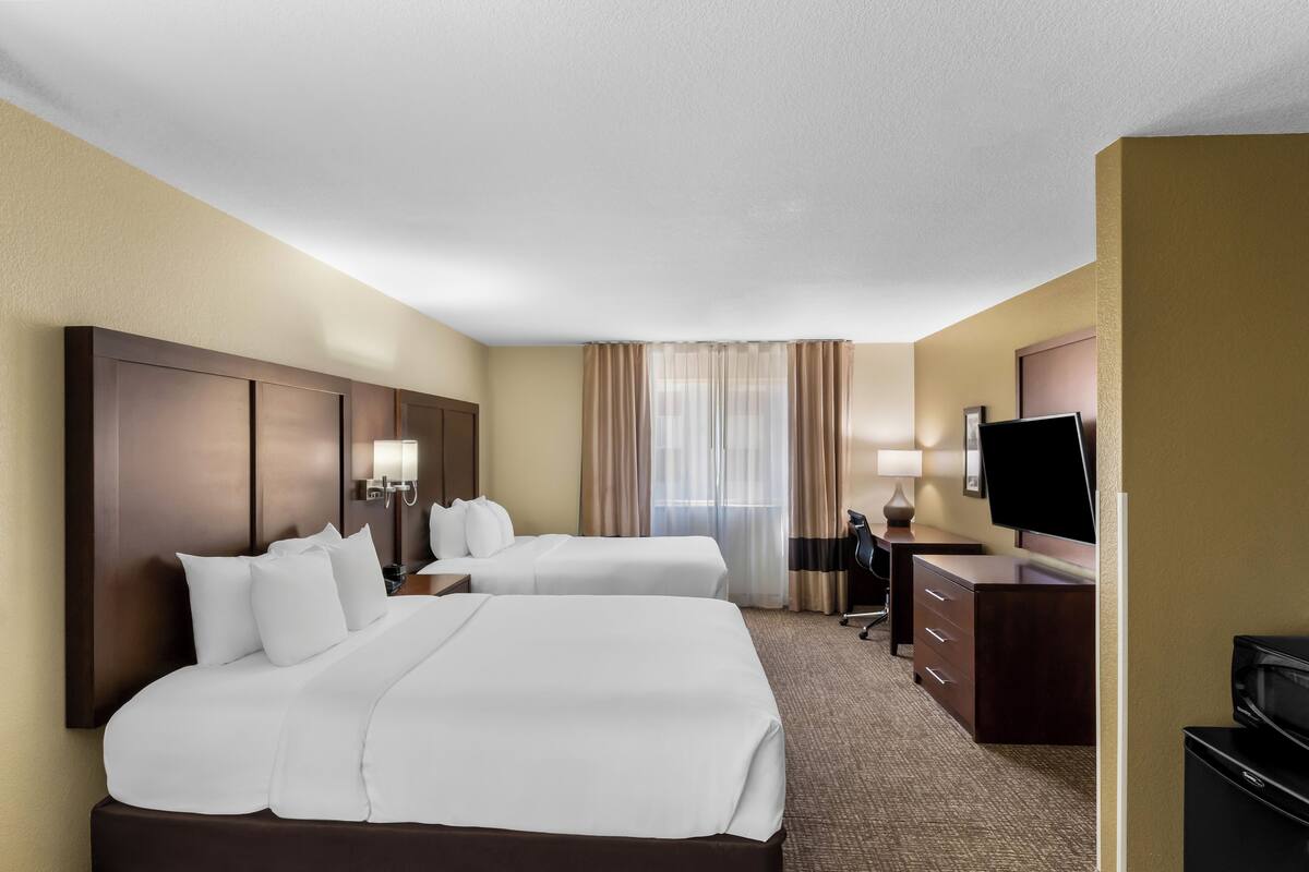 A hotel room with two beds, a desk, a TV, and a minibar.