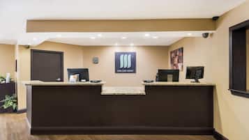 A reception desk with a "Live Like Home" sign, a security camera, and a framed artwork on the wall.
