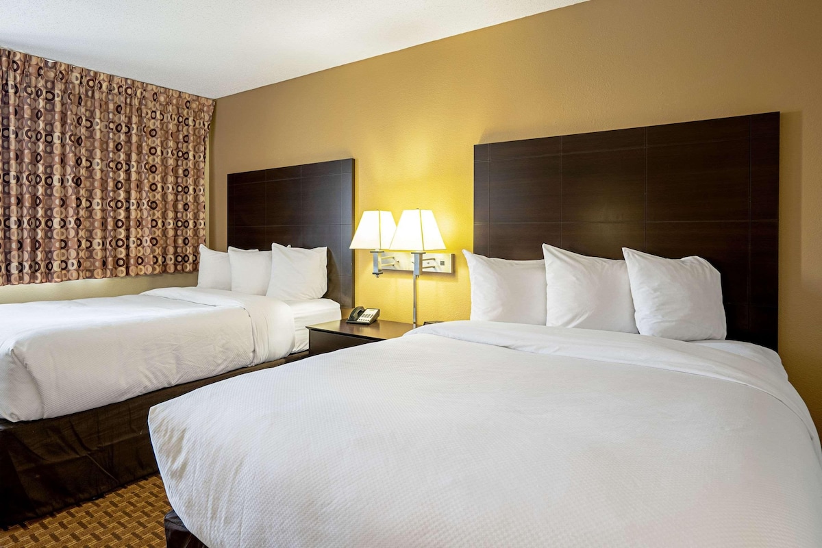 A hotel room with two beds, a nightstand with a lamp, and a patterned curtain.