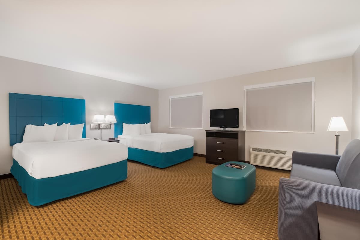 A hotel room with two beds, a TV, a desk, a chair, and a small ottoman.