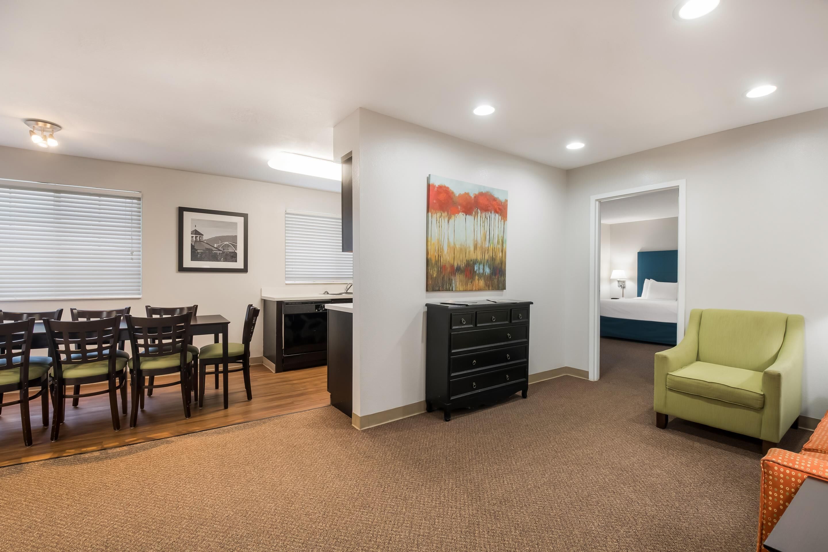 A modern living room with a dining area, a black dresser, a green armchair, and a painting on the wall.