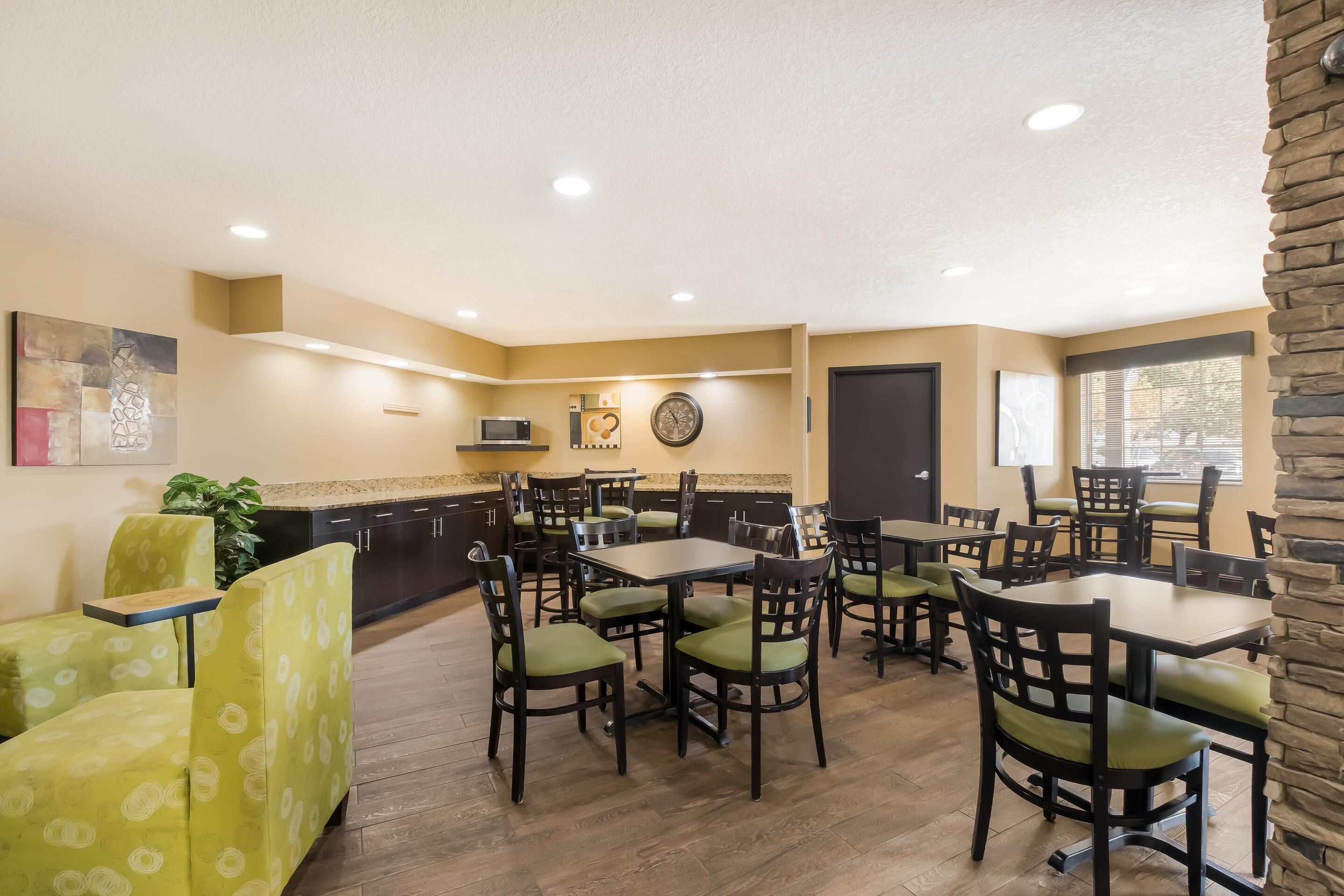 A dining area with multiple tables and chairs, a kitchen area with a microwave, and a clock on the wall.