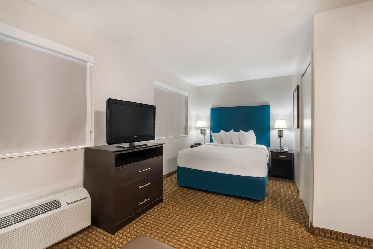 A hotel room with a bed, a TV, a dresser, a nightstand, and a lamp.