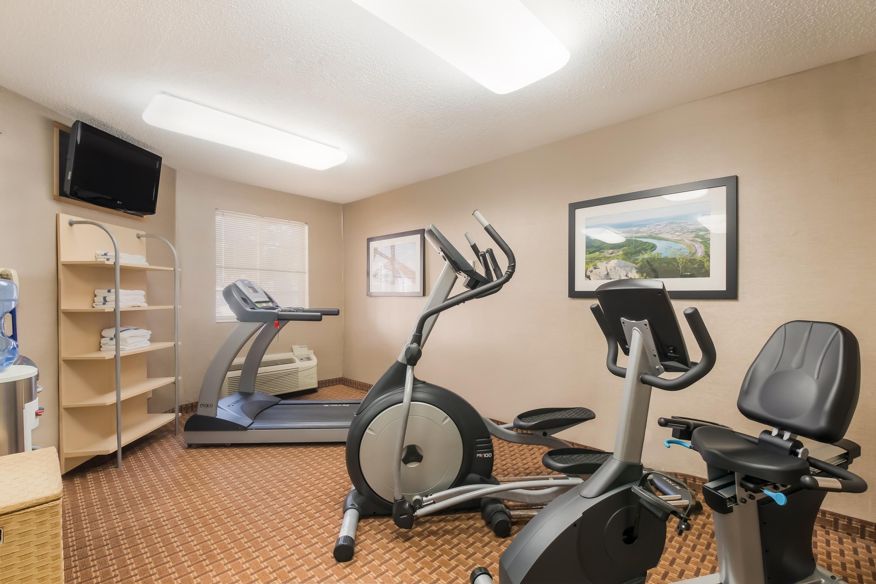 Un gimnasio con equipamiento de ejercicio, televisión y dispensador de agua.