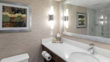 A modern bathroom with a sink, mirror, toilet, and framed artwork.