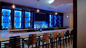 Una zona de bar con varias estanterías llenas de botellas, taburetes y lámparas colgantes.