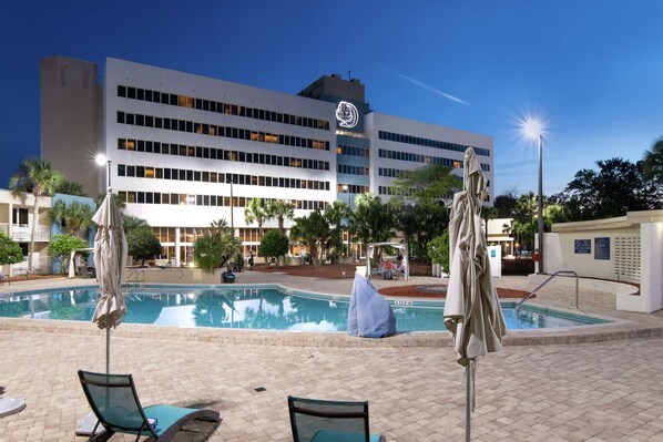 Un hotel con piscina, sillas de descanso y sombrillas.