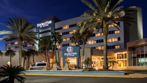 Un hotel DoubleTree by Hilton con una fachada moderna, palmeras y una entrada bien iluminada.