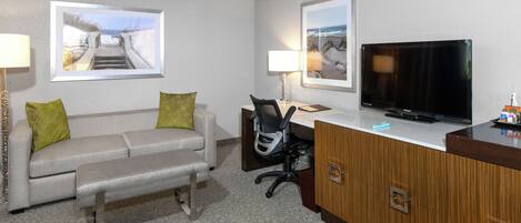 Habitación de hotel con sofá, banco, escritorio, televisor y cuadros en la pared.