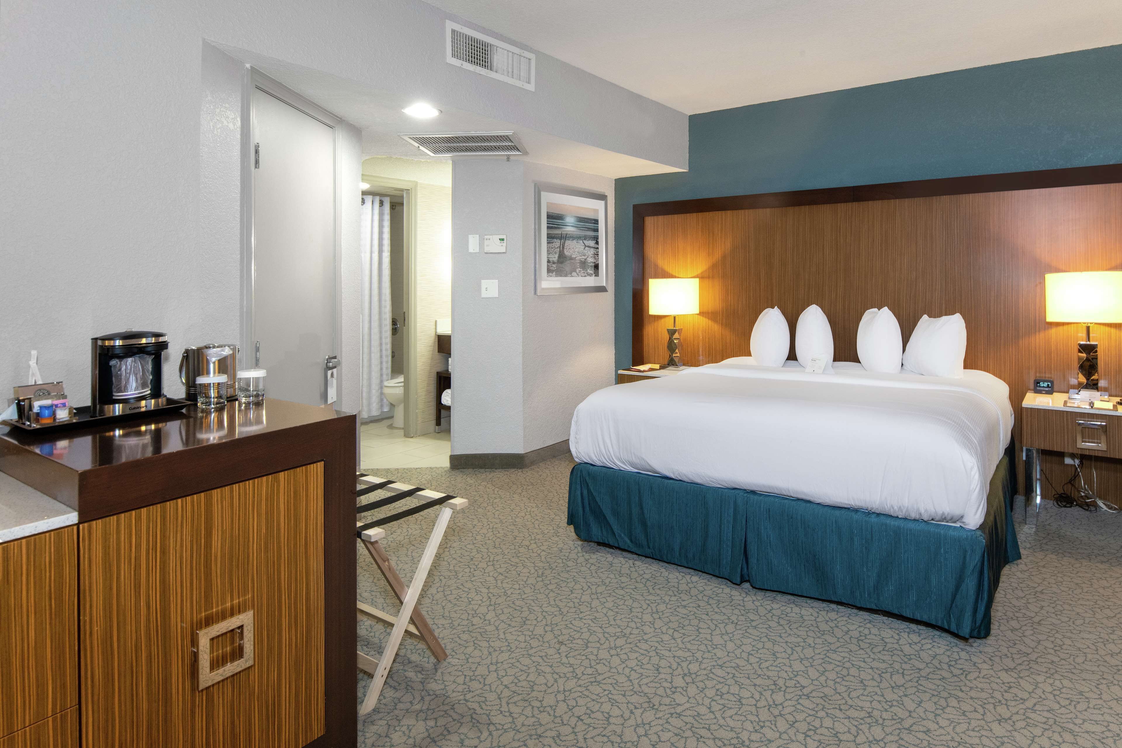 A hotel room with a large bed, a wooden desk, a chair, and a bathroom visible through an open door.
