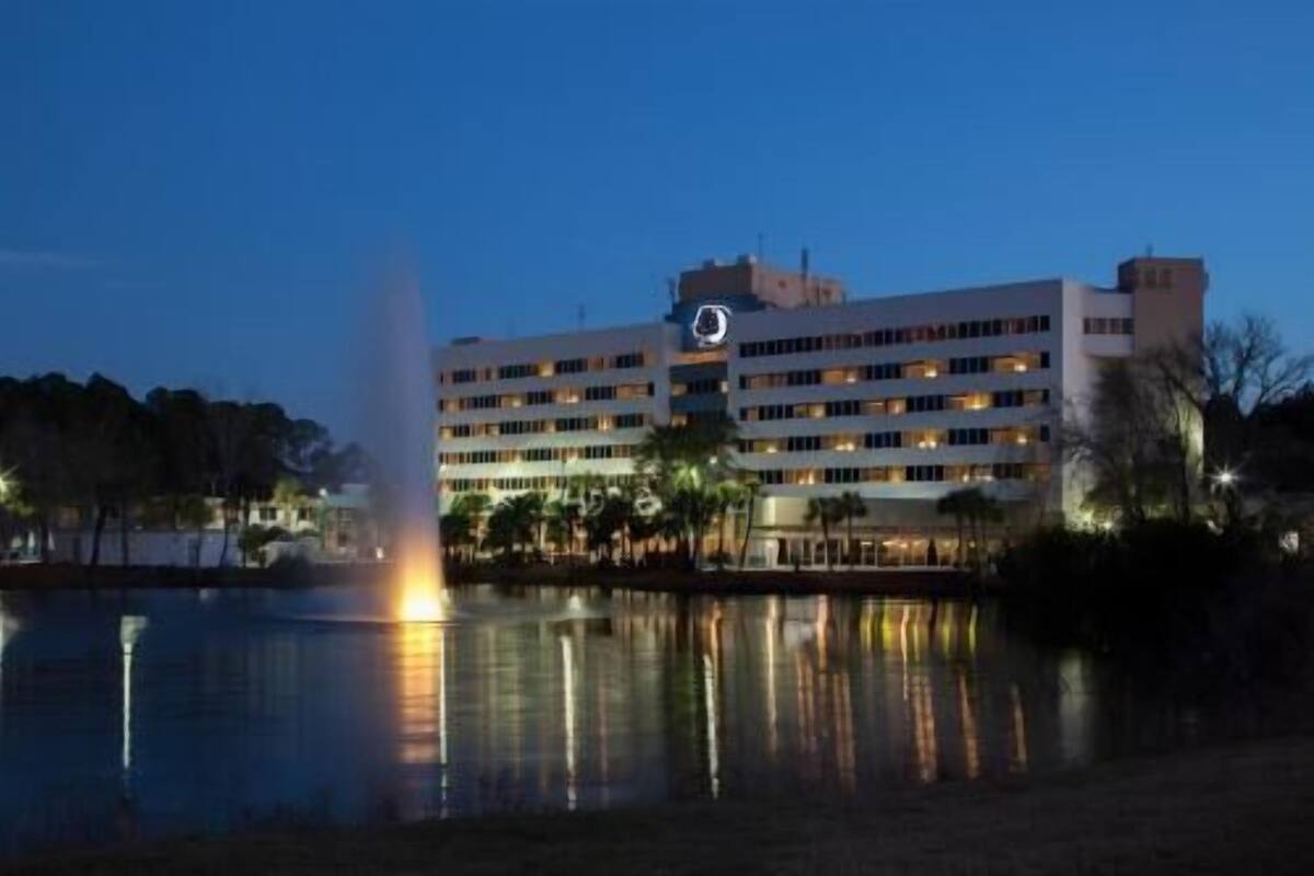 Un hotel a più piani con piscina e fontana, circondato da alberi.