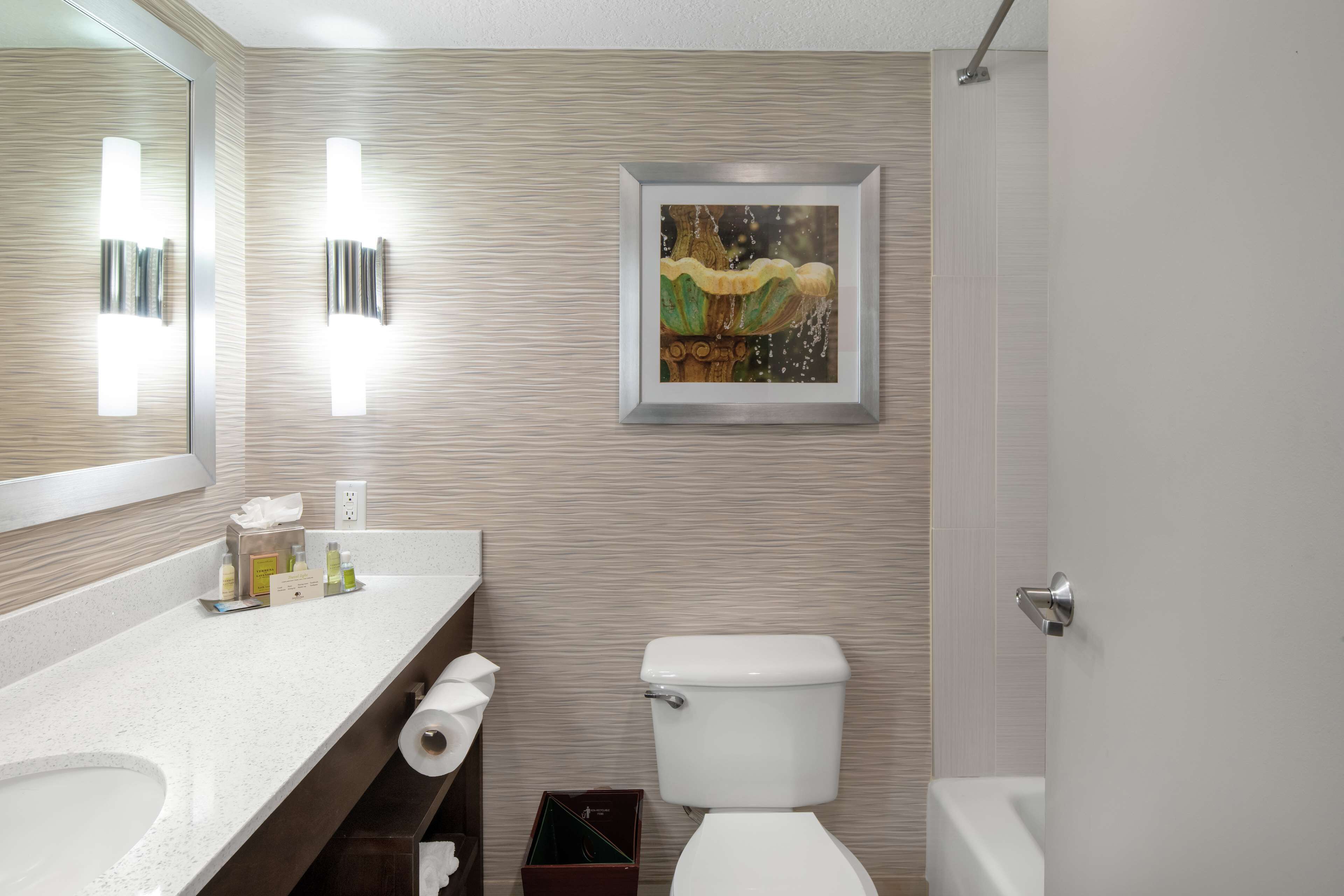 Un baño moderno con lavamanos, inodoro y ducha blancos. Hay un cuadro en la pared y un espejo sobre el lavamanos.