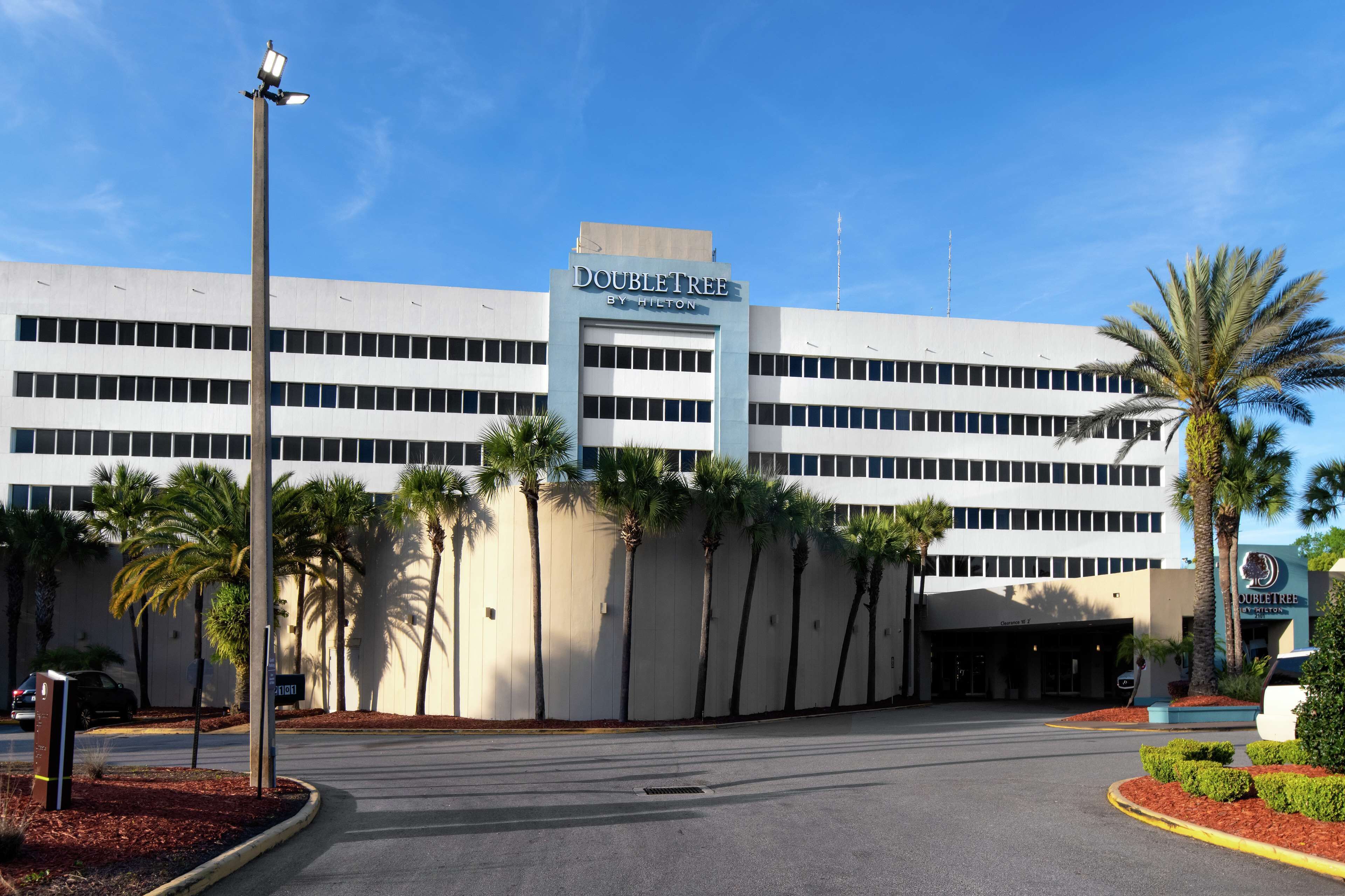 A DoubleTree by Hilton hotel with a modern design, palm trees, and a clear blue sky.