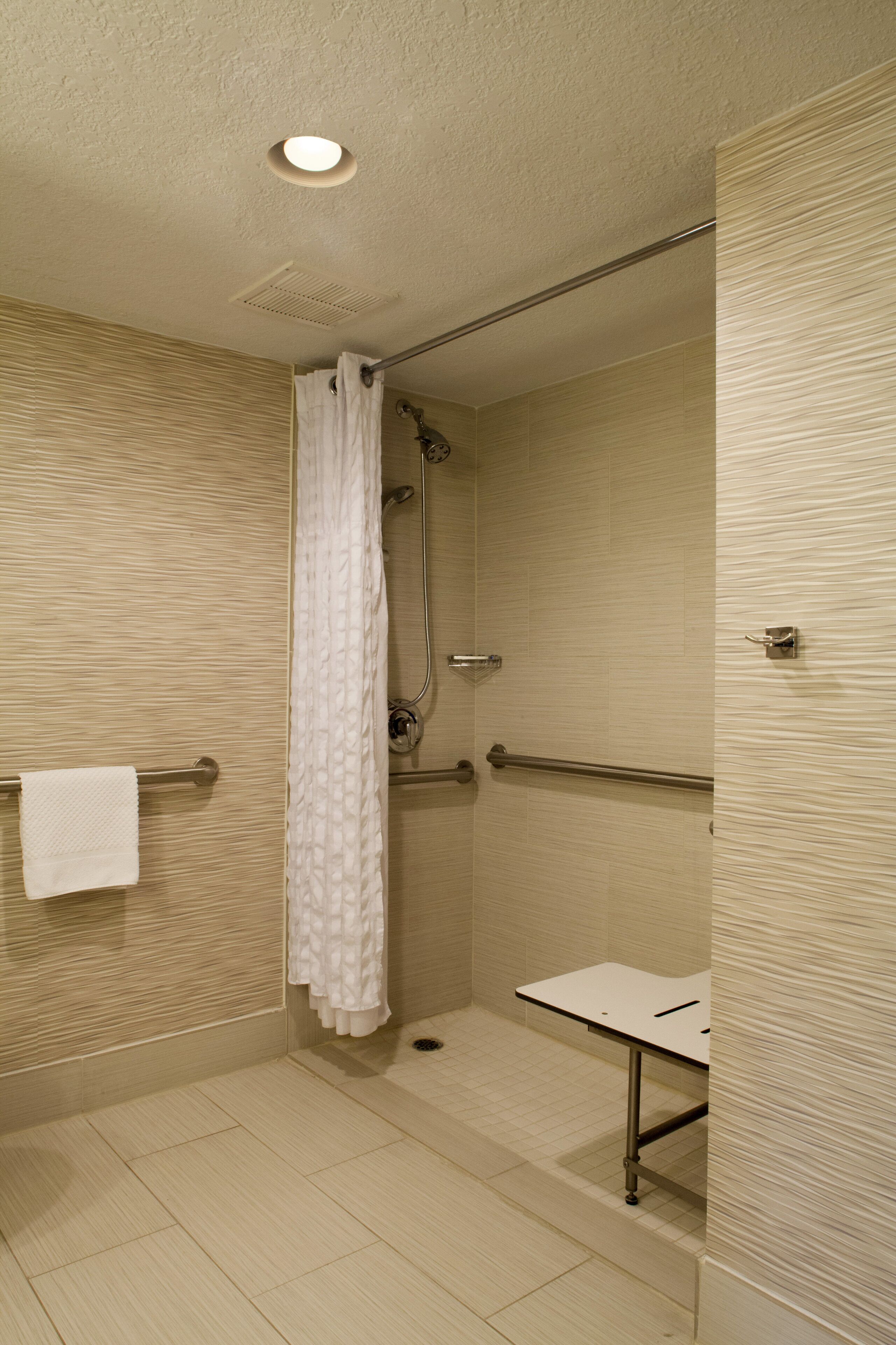 A small, enclosed shower area with a white shower curtain, a towel rack, and a grab bar.