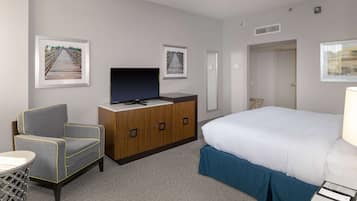 A hotel room with a bed, a TV on a wooden cabinet, a grey armchair, and two framed pictures on the wall.