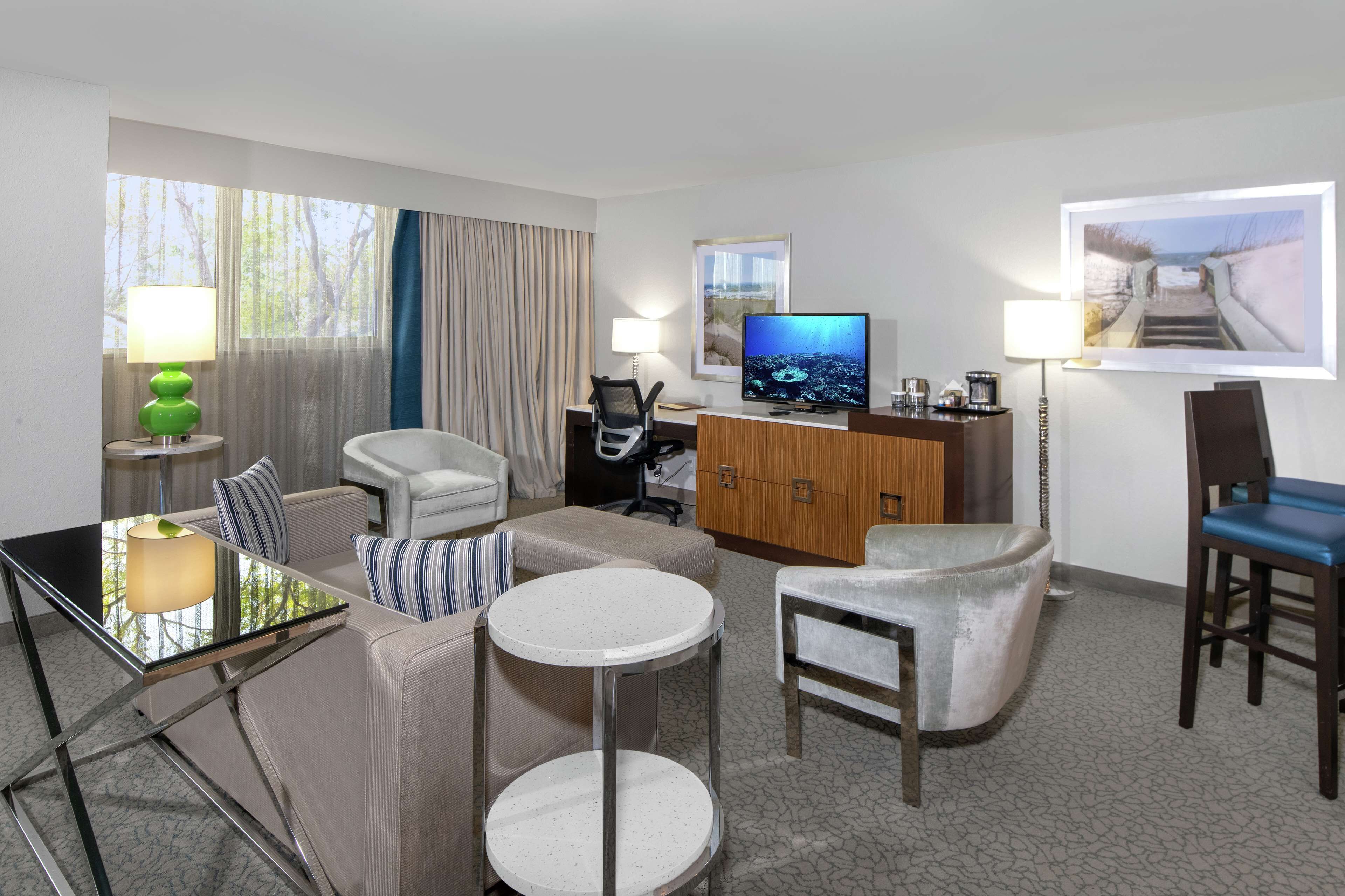Een hotelkamer met een bank, twee ronde tafels, een televisie, een kast en een bureau met een lamp.