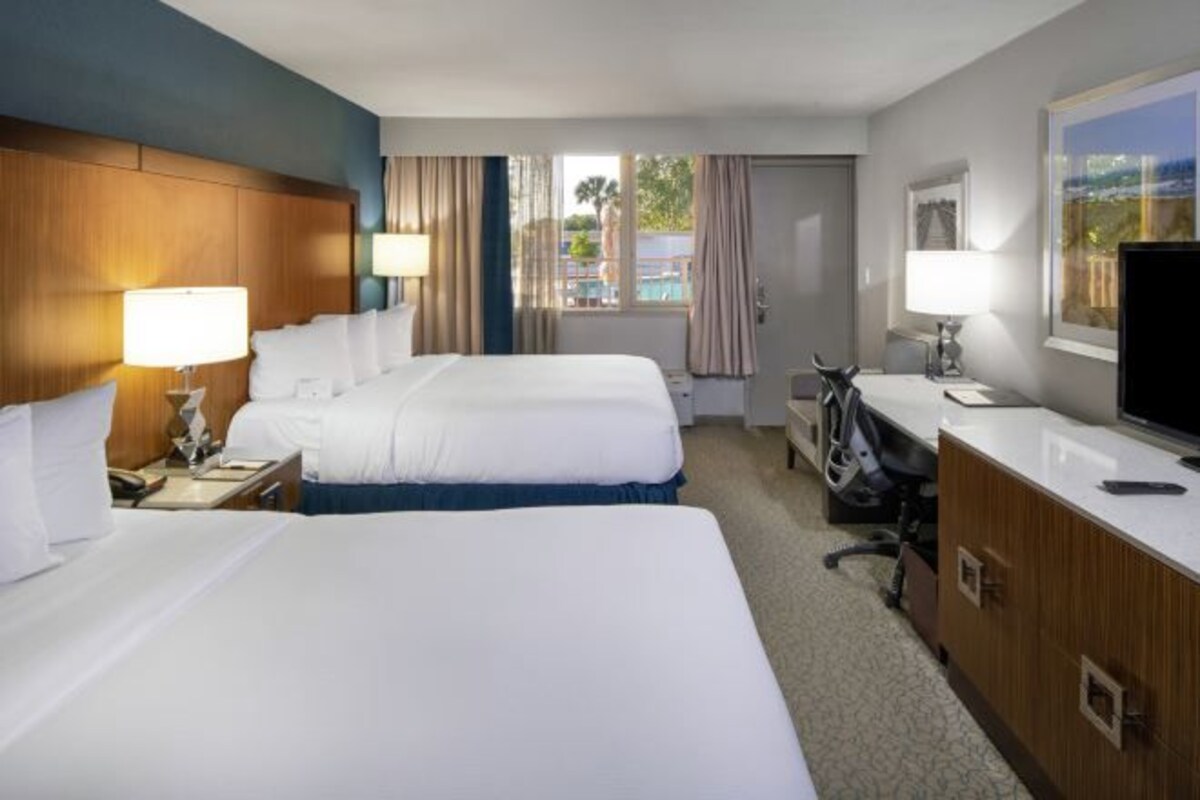 Habitación de hotel con dos camas, un escritorio, televisión y vistas al exterior.