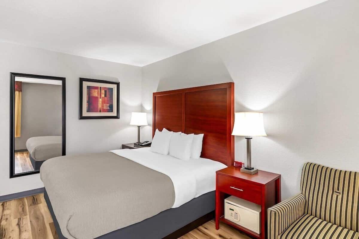 A hotel room with a bed, bedside tables, a lamp, a chair, and a mirror.