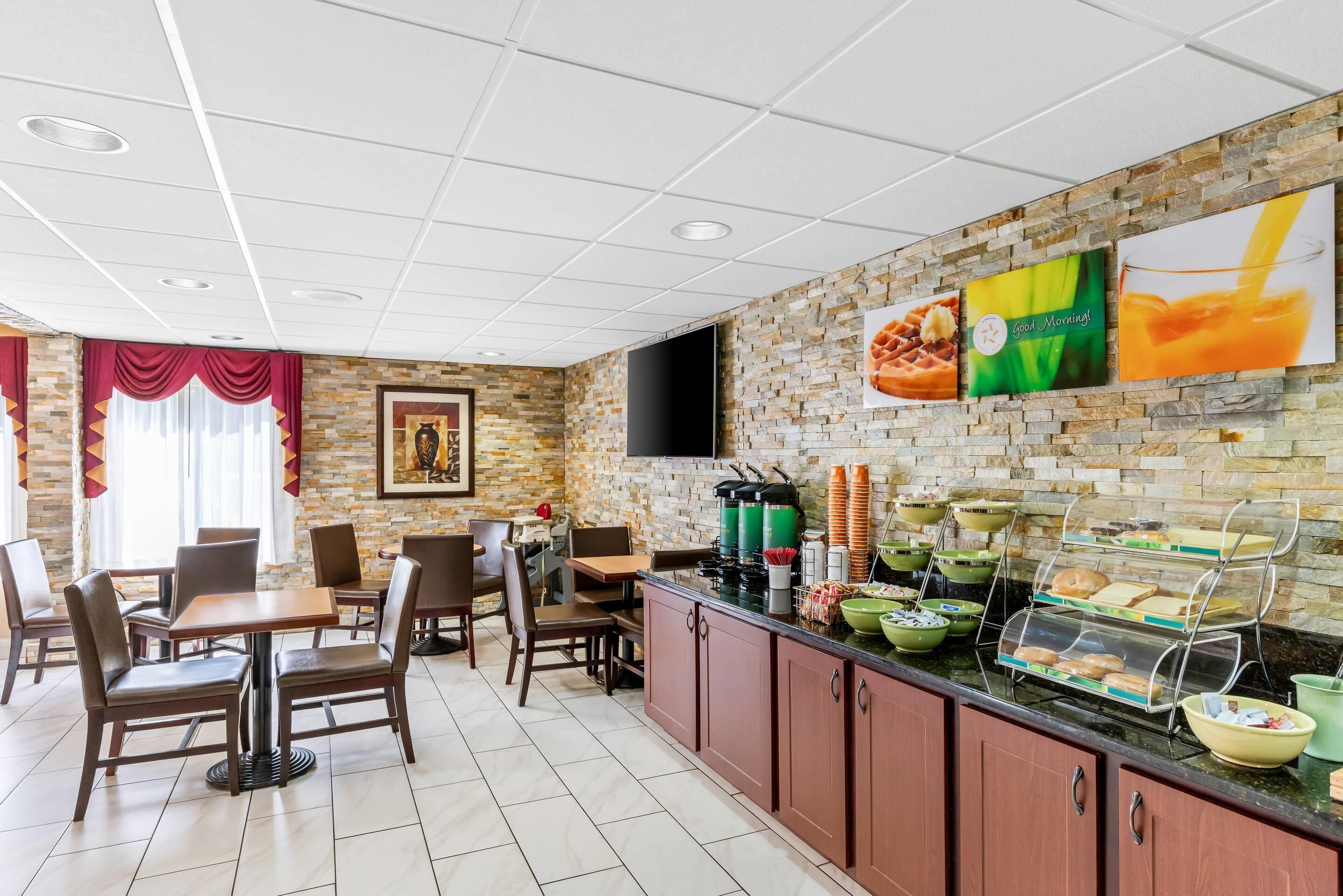 A restaurant with a brick wall, a buffet counter with various food items, and a television mounted on the wall.