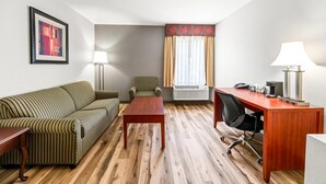 A hotel room with a striped sofa, a wooden coffee table, a desk with a chair, a lamp, and a framed picture on the wall.