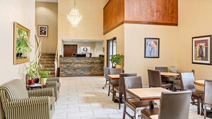 A hotel lobby with a reception desk, seating area, staircase, and decorative plants.