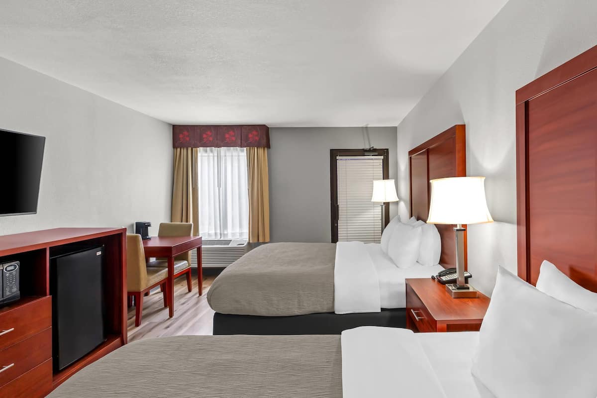 A hotel room with a bed, a desk with a computer, a chair, a TV, and a lamp.
